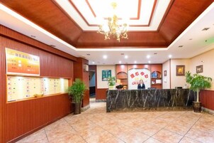 Zona de recepción de un hotel con mostrador de mármol, paneles de madera, una lámpara de araña y un escritorio para la recepción.