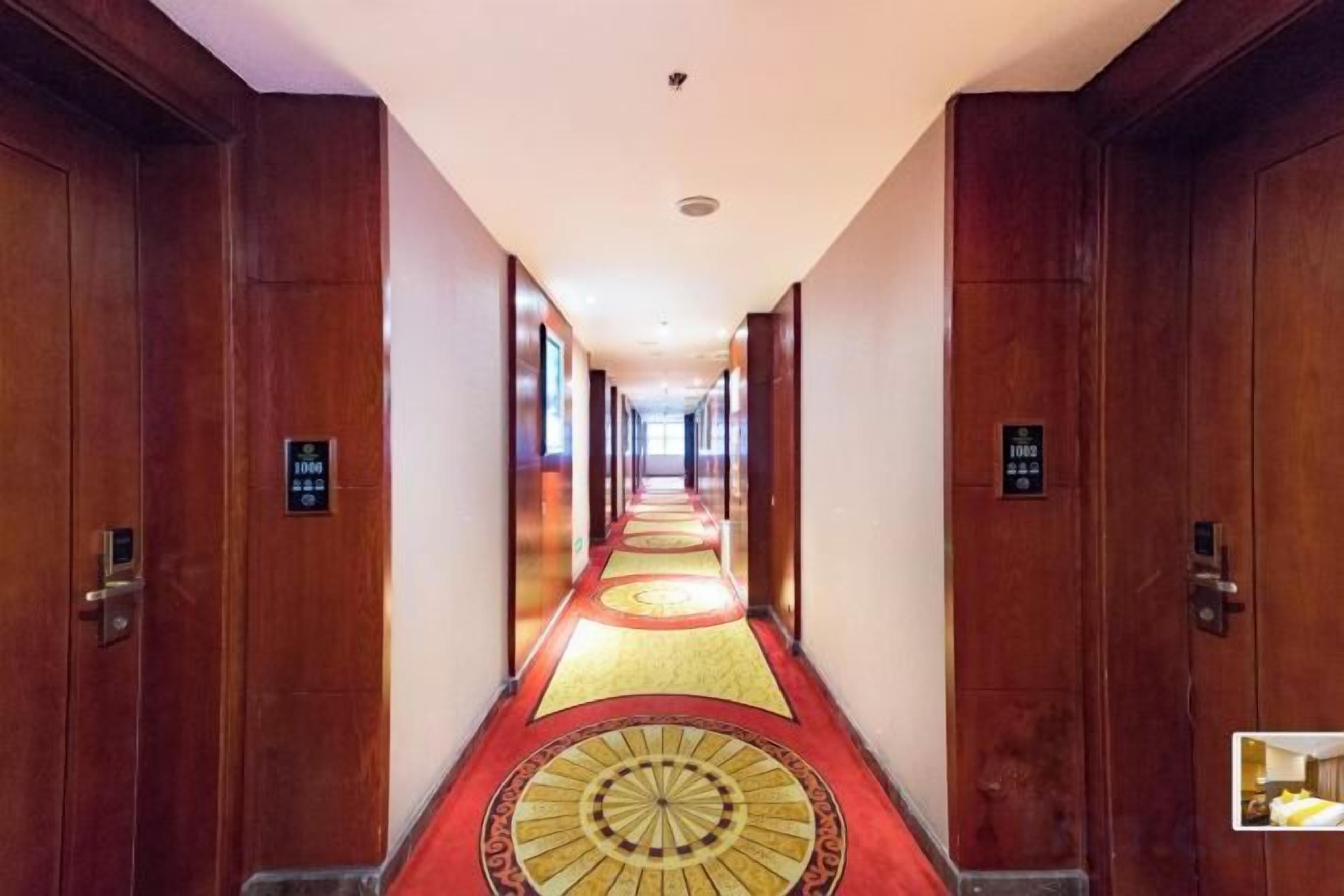A hotel corridor with wooden doors, a patterned carpet, and a sign indicating the direction to the elevator.