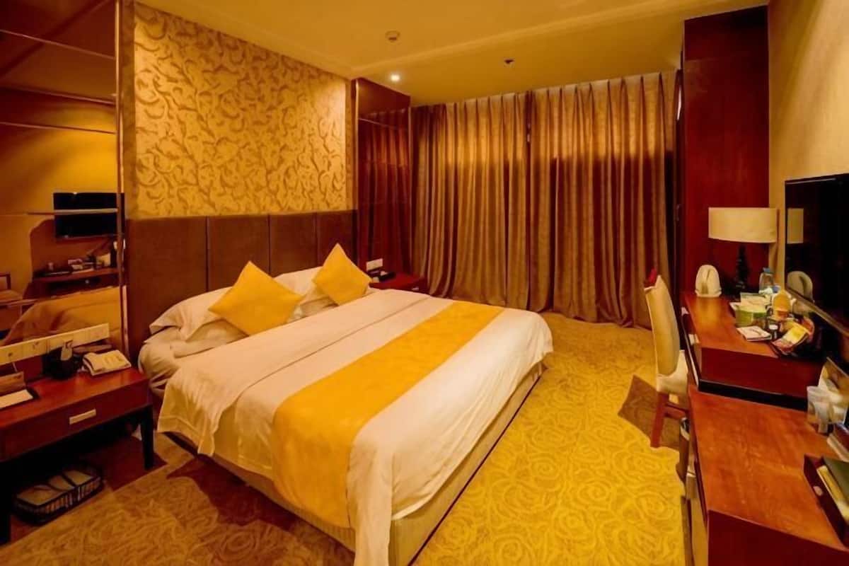 A hotel room with a large bed, a desk, a chair, a television, and a mirror.