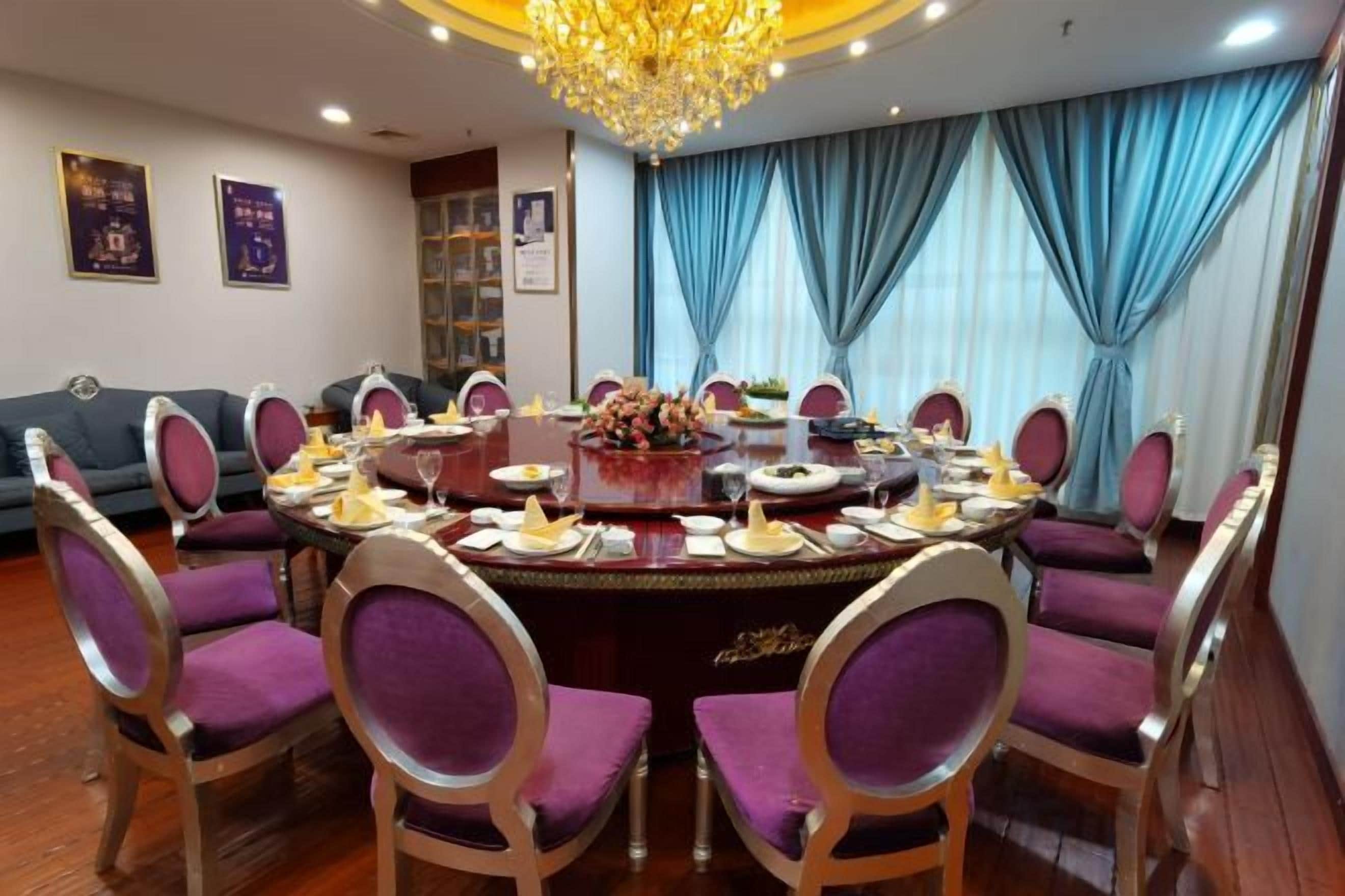 A formal dining room with a round table, purple chairs, and a chandelier.