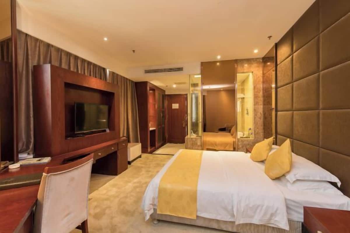 A hotel room with a large bed, a television, a desk, and a mirror.