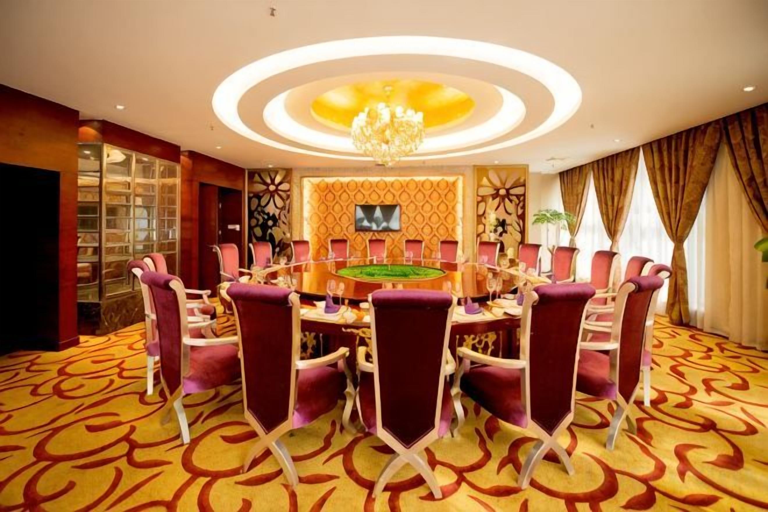 A conference room with a round table, chairs, a chandelier, and a television screen.
