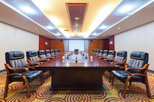 Un salón de conferencias con una larga mesa y sillas, una pantalla de proyector y suelo alfombrado.