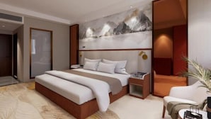 Una habitación de hotel moderna con una cama grande, una mesita de noche, una zona de estar y una pared decorada con un cuadro de un paisaje montañoso.
