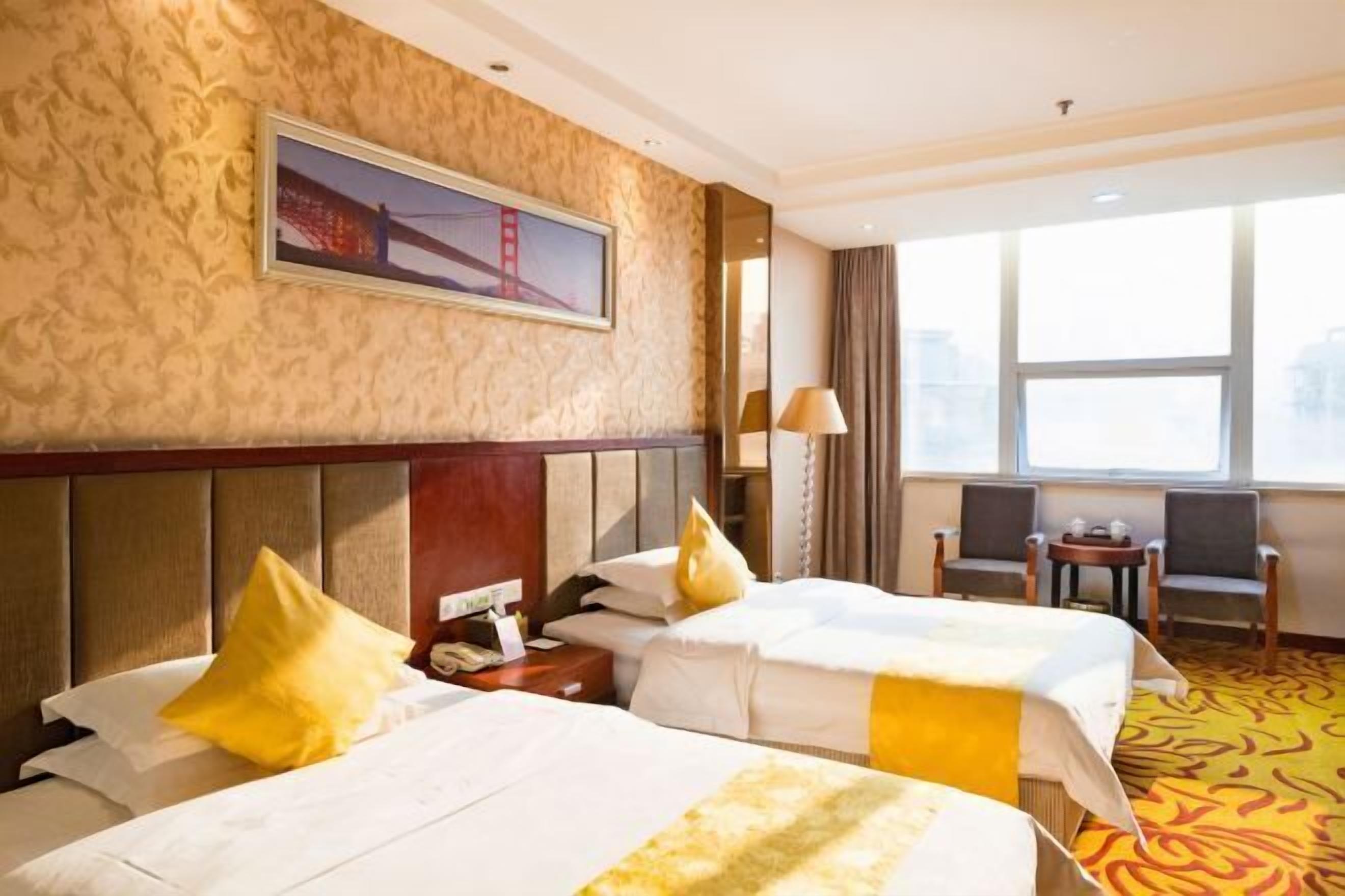 Habitación de hotel con dos camas, un ventanal grande, un cuadro de un puente y suelo alfombrado.