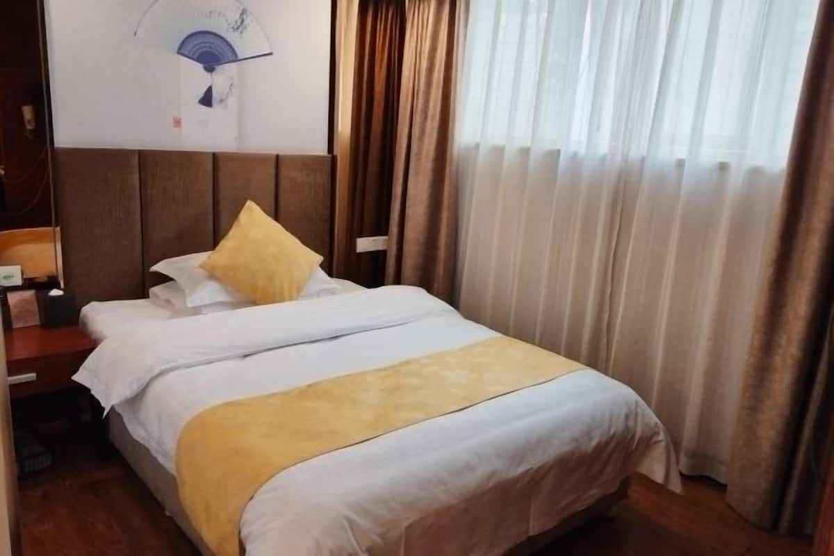 A hotel room with a bed, a nightstand, a wall clock, and a window with curtains.