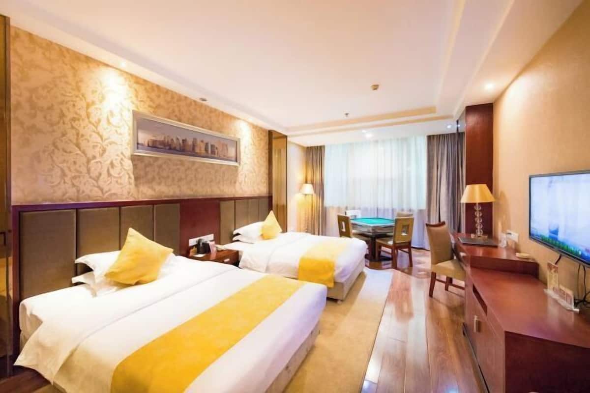 A hotel room with two beds, a desk, a TV, and a dining table.