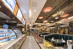 Un restaurante con mostrador central, zonas de estar y una vitrina con alimentos.
