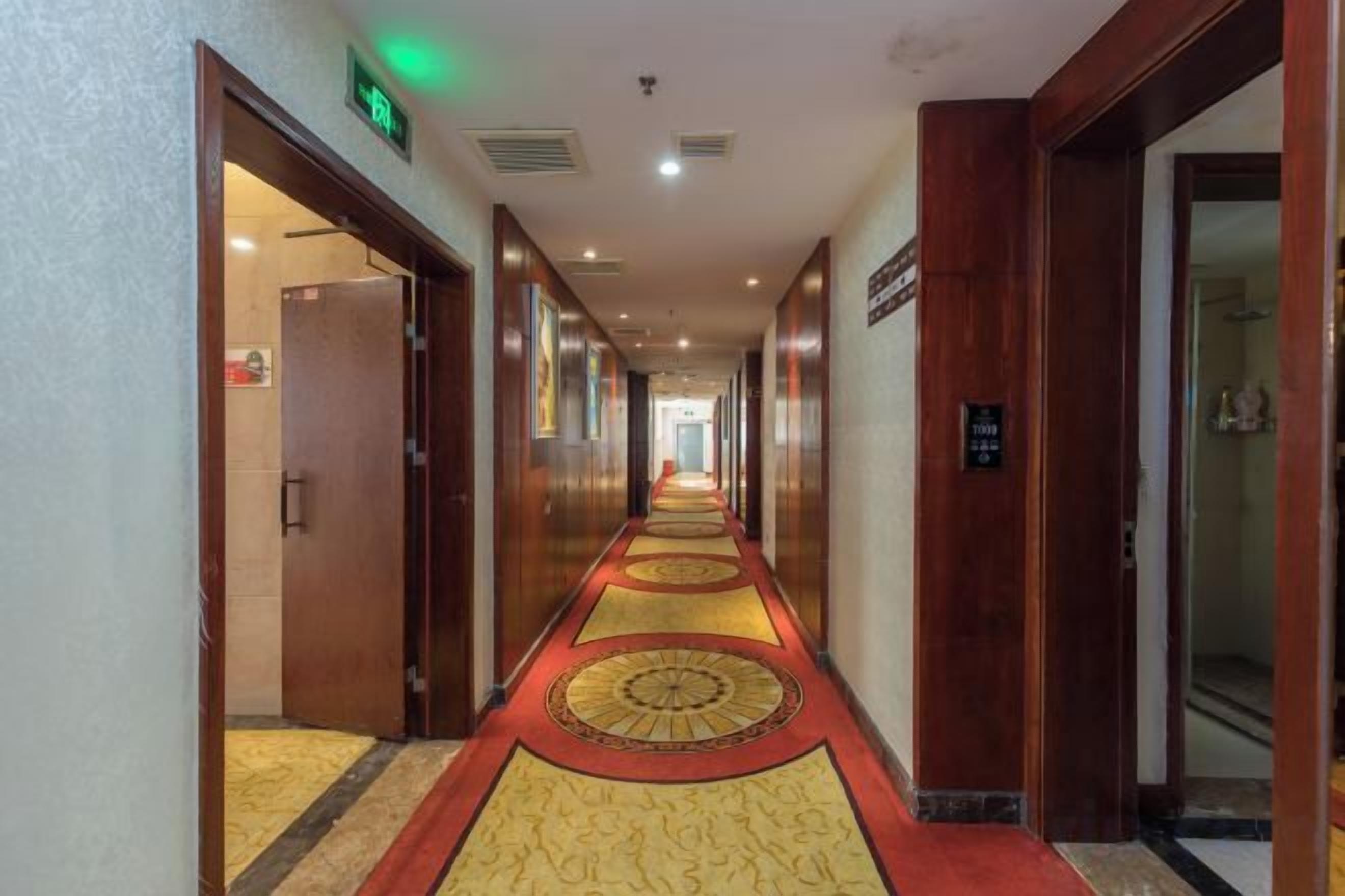 Pasillo de hotel con piso alfombrado, puertas a ambos lados y una señal que indica la dirección al ascensor.