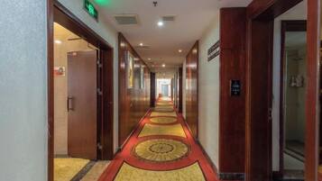 Pasillo de hotel con piso alfombrado, puertas a ambos lados y una señal que indica la dirección al ascensor.