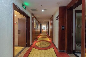 Pasillo de hotel con piso alfombrado, puertas a ambos lados y una señal que indica la dirección al ascensor.