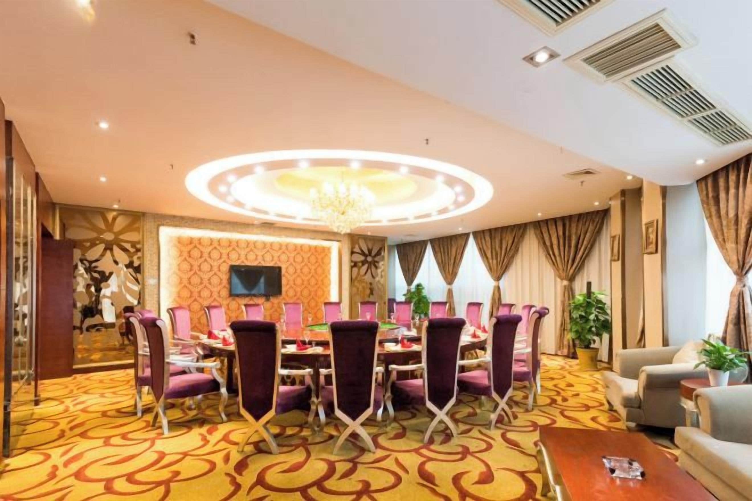 Un salón de conferencias de hotel con una mesa redonda, sillas moradas, una araña y una alfombra estampada.
