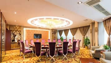 Ein Hotelkonferenzraum mit einem runden Tisch, violetten Stühlen, einer Chandelüster und einem gemusterten Teppich.