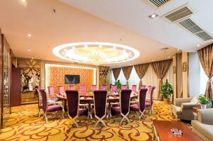 Un salón de conferencias de hotel con una mesa redonda, sillas moradas, una araña y una alfombra estampada.