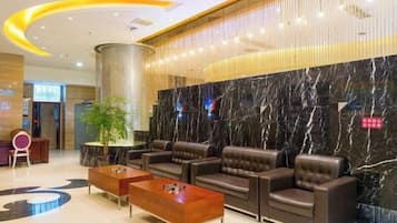 Eine Hotelhalle mit Empfangstresen, Sitzgelegenheiten und einer großen Marmorwand.