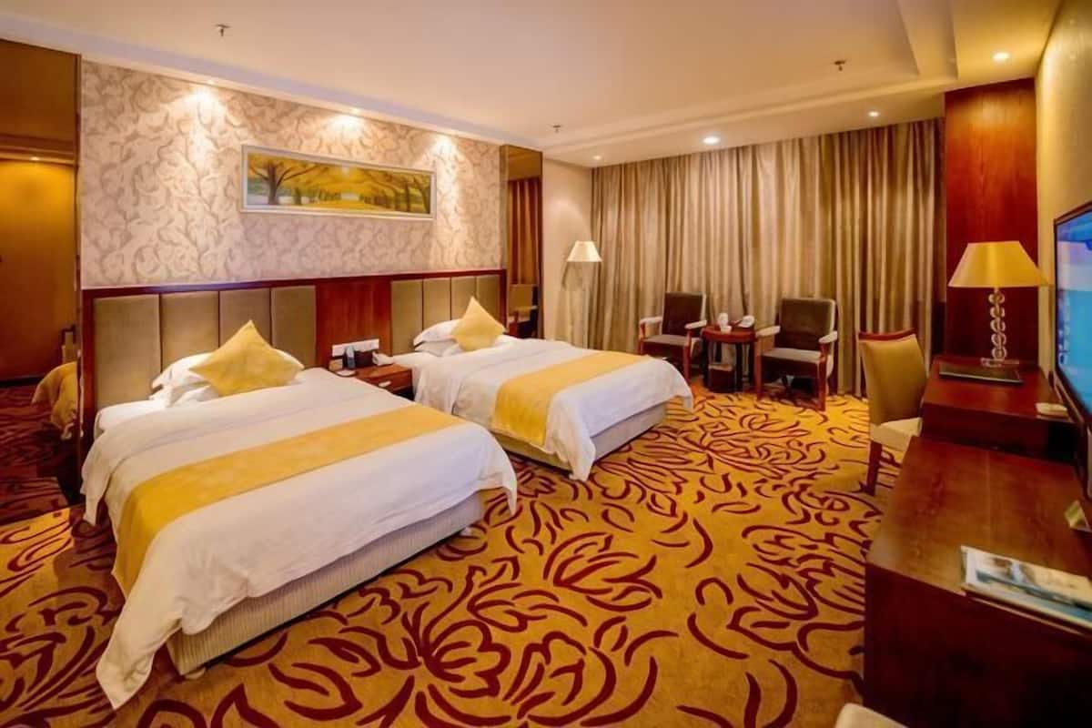 A hotel room with two beds, a desk, a chair, a TV, and a large window with curtains.