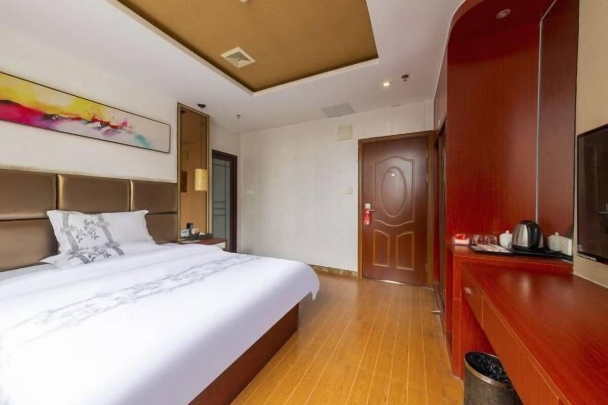 A hotel room with a bed, a desk with a chair, a television, and a door.