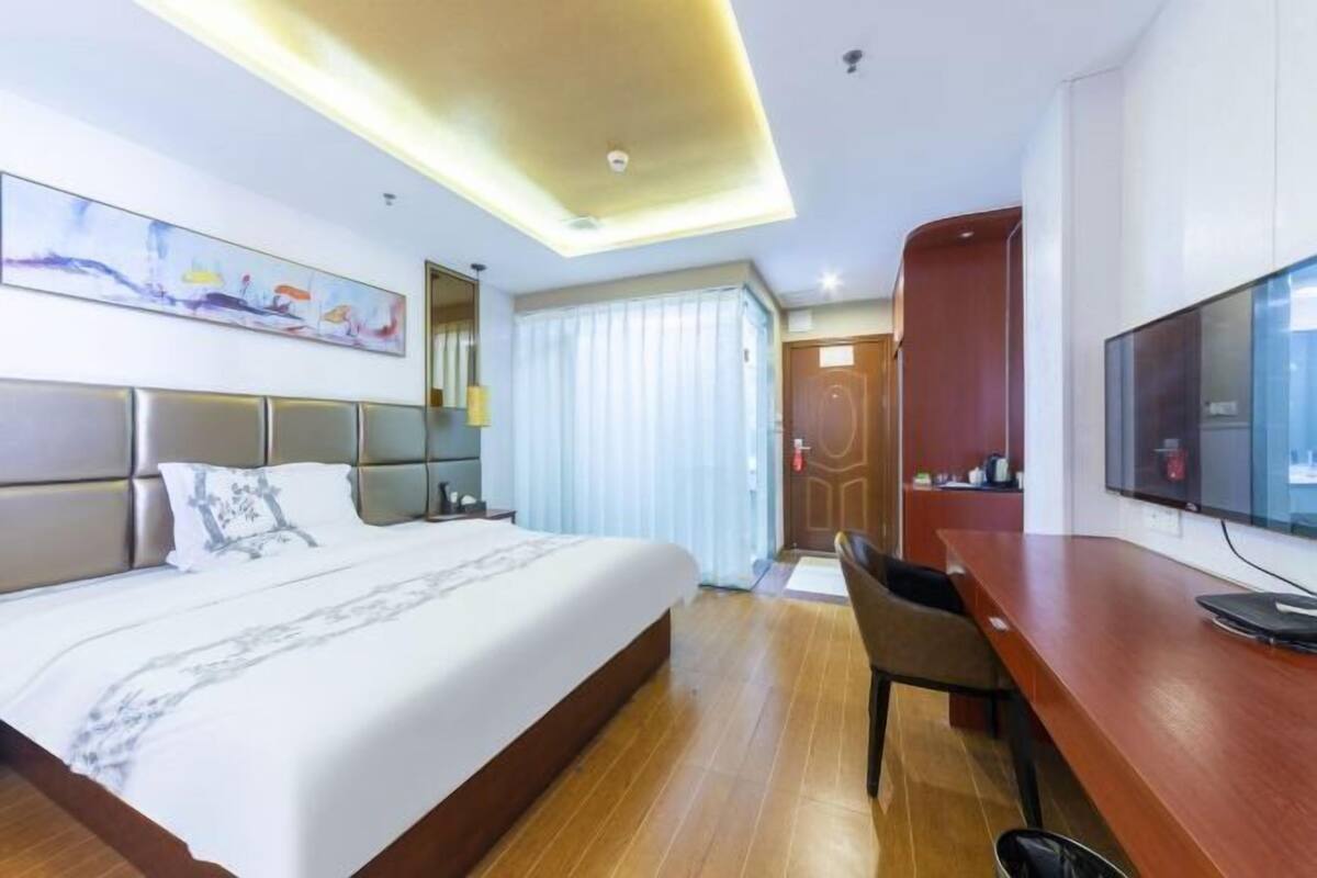 A hotel room with a bed, a desk, a chair, a television, and a painting on the wall.