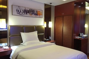 A hotel room with a bed, a nightstand, a wooden wardrobe, and a painting on the wall. - Guanghe Business Hotel (Shaoguan Fengcai Experimental School) (Shaoguan)