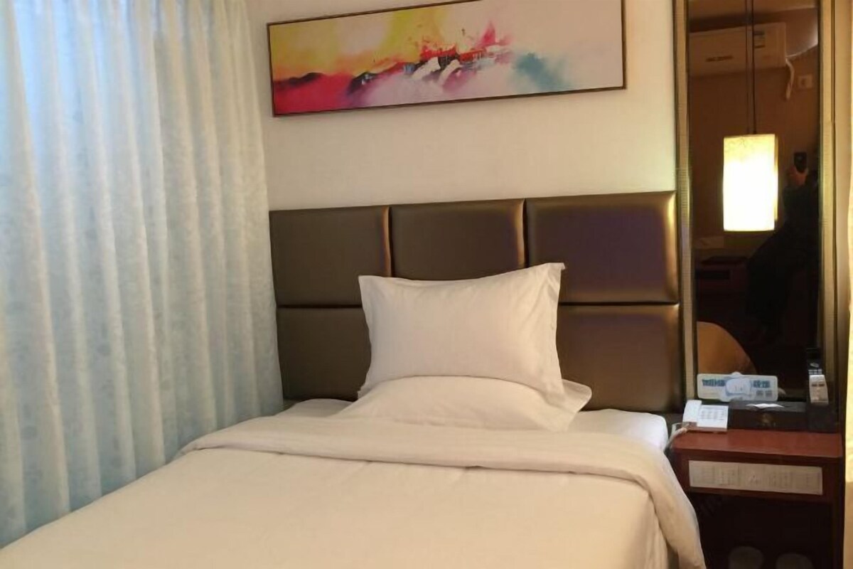 A hotel room with a bed, a headboard, a bedside table, a lamp, and a painting on the wall.
