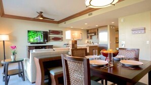 Un coin repas avec une table en bois dressée pour quatre personnes, un téléviseur fixé au mur et un ventilateur de plafond.