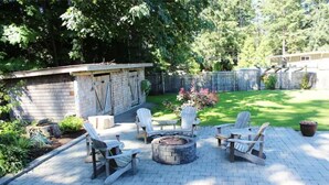 A patio area with a fire pit and Adirondack chairs.