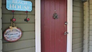 A red door with a small wreath on the doorknob and a blue sign above it that reads "BEACH HOUSE".