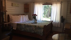 A bedroom with a bed, a bedside table, a lamp, a window with curtains, and a view of greenery outside.