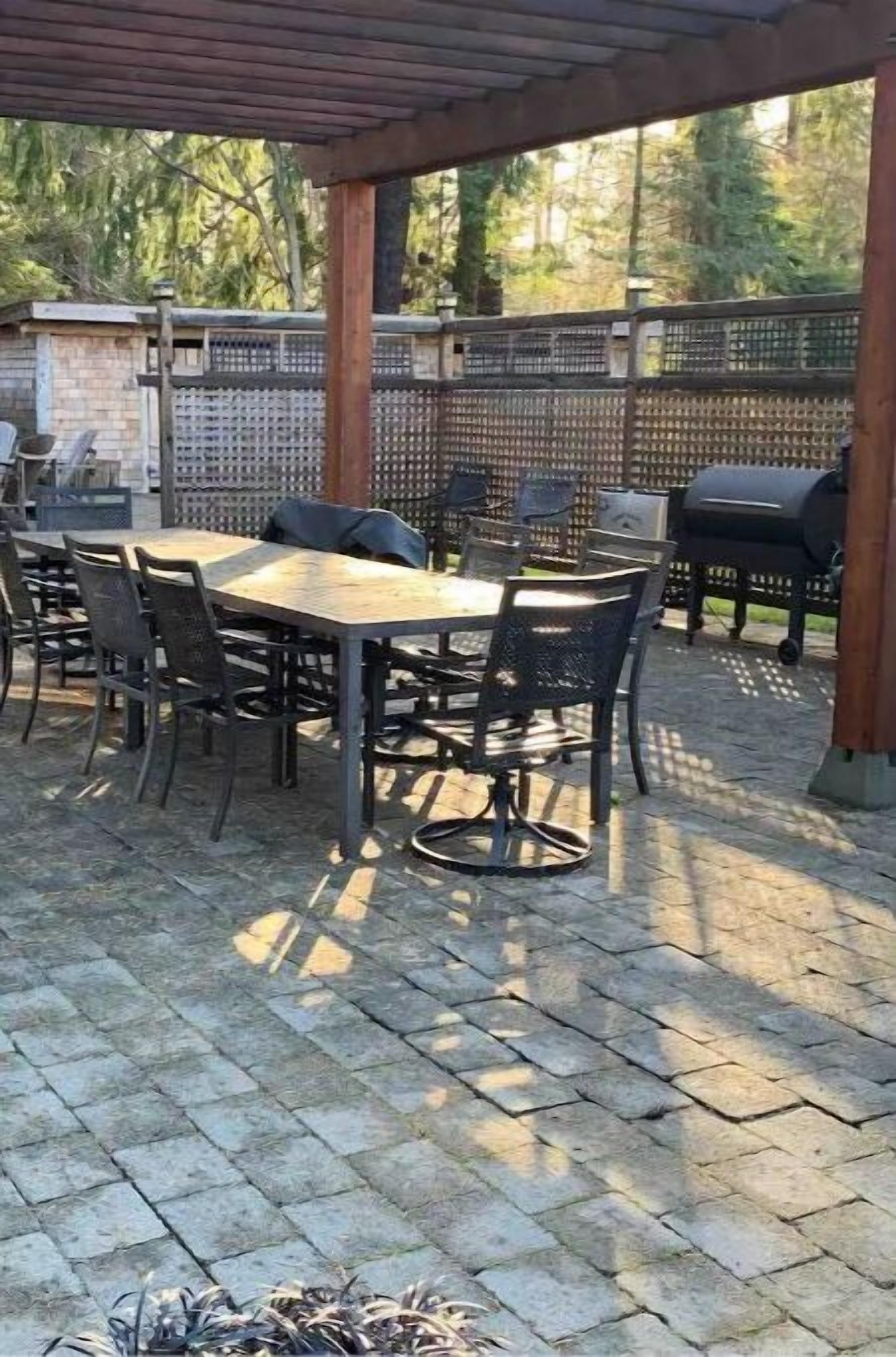 An outdoor patio with a wooden table and chairs, a grill, and a covered seating area.