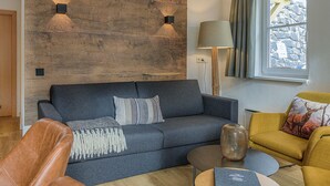 Una sala de estar moderna con un sofá gris oscuro, un sillón amarillo, una mesa de centro de madera y una pared de piedra.