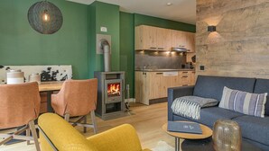 Una sala de estar acogedora con sofá, sillas, una mesita de centro, chimenea y una cocina con armarios de madera.