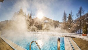 Una piscina termal con agua cristalina, rodeada por una terraza de madera y suelo cubierto de nieve.