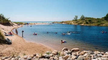 Une plage où l’on voit des gens nager et flotter, un rivage sablonneux et un premier plan rocheux.