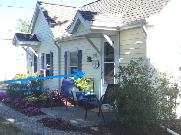 A two-story house with a porch, blue shutters, and a welcome sign. There are two blue chairs on the porch.