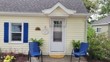 A house with a front door, two blue chairs, and a small sign above the door.