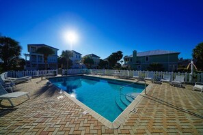 Ein rechteckiger Swimmingpool mit weißem Zaun, umgeben von Liegestühlen und einer gepflasterten Terrasse.