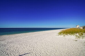 A beach with white sand, clear blue water, and buildings in the background. - The Purple Sunset-200ft to Beach w Pool (Navarre)