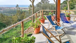 A terrace with wooden railings, potted plants, and blue lounge chairs overlooking a coastal landscape. - Gorgeous home in Ascea Marina with house sea view (Ascea Marina)
