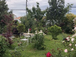 A garden with a white metal table and chair, surrounded by various plants and flowers.
