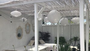A covered outdoor seating area with white furniture, decorative mirrors, and hanging paper lanterns. - Small warm house. (Le Château-d'Oléron)
