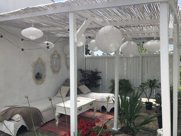 A covered outdoor seating area with white furniture, decorative mirrors, and hanging paper lanterns.