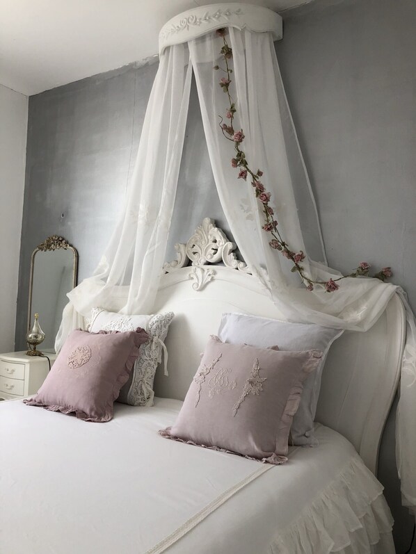 A bedroom with a canopy bed, white bedding, and decorative pillows.
