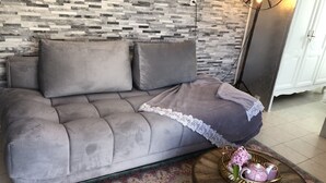 A grey sofa with a lace throw, a wooden coffee table with a decorative tray, and a patterned rug. - Small warm house. (Le Château-d'Oléron)