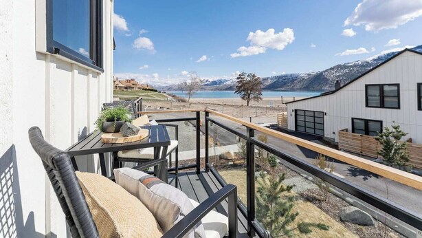 Varanda com mesa e cadeiras, vista para uma praia e montanhas.