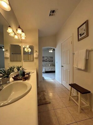 Un pasillo estrecho con un baño a la izquierda, un banco a la derecha y un dormitorio al final.