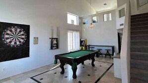 Ein geräumiges Zimmer mit Billardtisch, Dartscheibe und einer Treppe.