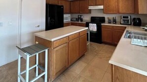 Eine kleine Küche mit Holzschränken, einer weißen Arbeitsplatte, einem eingebauten Backofen und einer Edelstahlspüle.