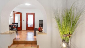 A hallway with a staircase leading to a room, a desk with a chair, a red vase, and a tall plant with a lantern.