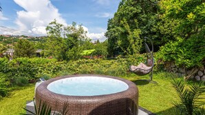 A hot tub in a lush garden with a hanging chair and a stone wall.