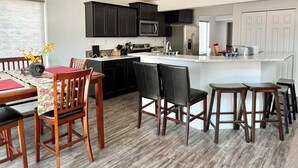 Una cocina moderna con armarios oscuros, una isla central y un comedor con sillas y mesa de madera.